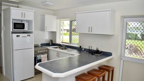 Une cuisine moderne avec des meubles blancs, un four à micro-ondes encastré, une cuisinière et un grand îlot central doté de tabourets de bar.