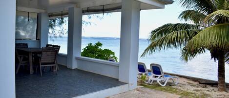 A covered outdoor area with a table and chairs, a view of the sea, and a palm tree.