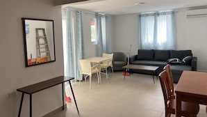 Ett modernt vardagsrum med en soffa, ett matbord och ett soffbord. En stege står lutad mot väggen och en kvast ligger på golvet.