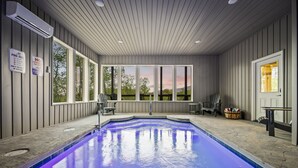 Piscina coberta com vista para o exterior, uma espreguiçadeira à beira da piscina e uma cesta com objetos.