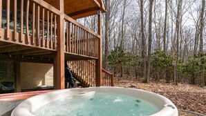 Ein Whirlpool auf einer Holzterrasse mit Blick auf einen Wald.