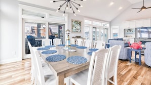 A spacious dining area with a wooden table, white chairs, and blue placemats. - Beach Blessings | 950 ft to the beach | Private Pool, Hot Tub, Community Pool (Corolla)