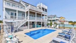 A two-story building with a swimming pool, outdoor seating, and a covered patio area. - Beach Blessings | 950 ft to the beach | Private Pool, Hot Tub, Community Pool (Corolla)