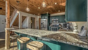Une cuisine dotée d’un plan de travail en granit, d’appareils électroménagers en acier inoxydable, de meubles de couleur turquoise et d’un escalier en bois.