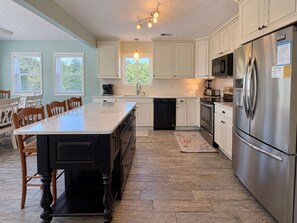 A spacious kitchen with a central island, stainless steel appliances, and a view of the outdoors through large windows.