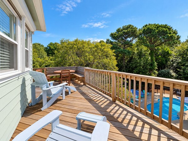 A wooden deck with outdoor furniture, a pool, and a view of trees.