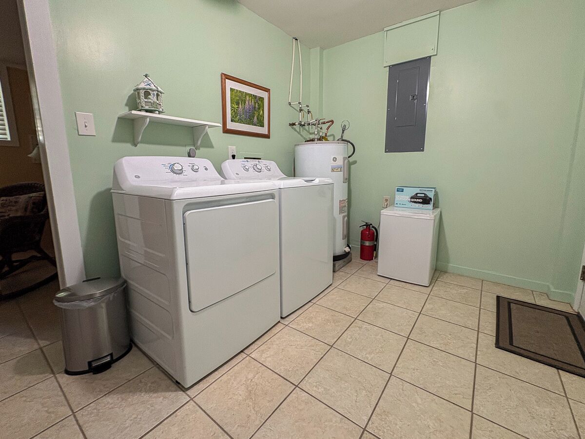 A laundry room with two stacked washers and dryers, a small trash can, a fire extinguisher, and a water heater.