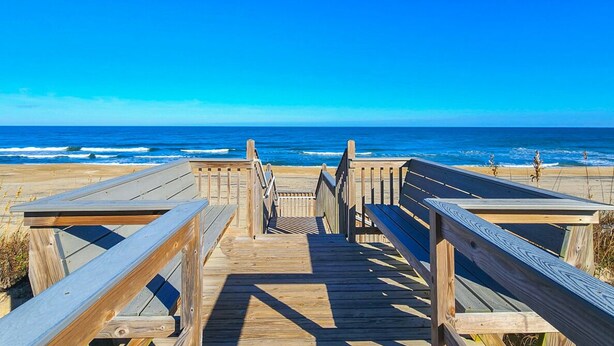 A wooden boardwalk leading to a beach with a clear blue sky.