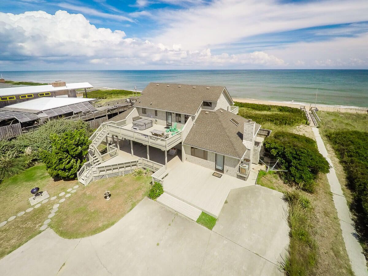 A two-story house with a large deck, a covered patio, and a view of the ocean.