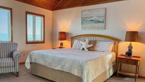 A bedroom with a large bed, two bedside lamps, a chair, and a painting on the wall.