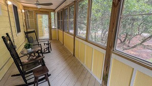 A covered porch with wooden flooring, yellow wainscoting, and large windows offering a view of trees. - SALTY PAUSE - Enjoy vacation paradise on the sound side in the 4 BR home w/Private Pool (Southern Shores)