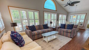 A spacious living room with a high ceiling, large windows, and a ceiling fan. - SALTY PAUSE - Enjoy vacation paradise on the sound side in the 4 BR home w/Private Pool (Southern Shores)