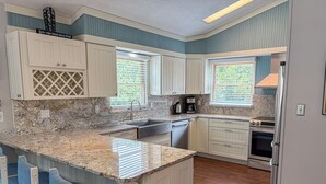 A kitchen with white cabinets, a granite countertop, a built-in island with bar stools, a stove, and a refrigerator. - SALTY PAUSE - Enjoy vacation paradise on the sound side in the 4 BR home w/Private Pool (Southern Shores)