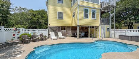 A two-story yellow house with a swimming pool, outdoor seating, and a covered patio area.