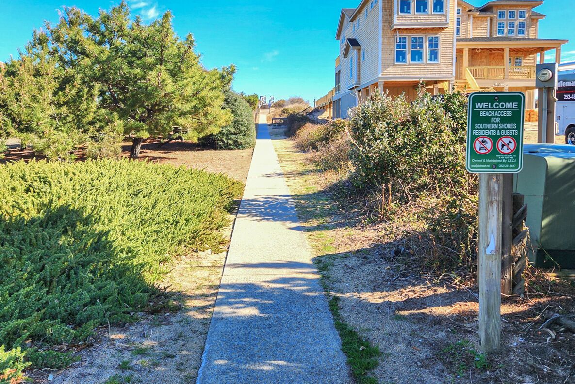 Ein Weg, der zu einem Gebäude führt, mit einem Schild, das Strandzugang für Bewohner und Gäste anzeigt.