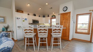 A kitchen with white cabinets, a microwave, and a wooden door. There are three white chairs with a wavy design. - Duckaway Home - Unwind in this 5 BR oceanside home in Duck w/Private Pool! (Duck)