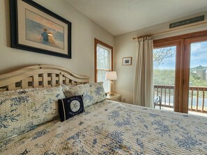 Ein Schlafzimmer mit einem großen Bett, einem gerahmten Gemälde, einem Fenster mit Vorhängen und Blick ins Freie.