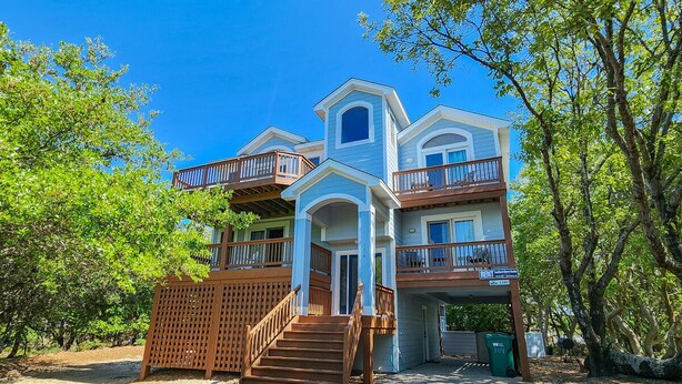 A two-story house with a front porch, wooden stairs, and a fenced yard. - Duckaway Home - Unwind in this 5 BR oceanside home in Duck w/Private Pool! (Duck)