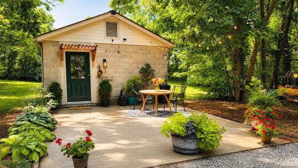 A small, single-story building with a green door, a patio with a table and chairs, and potted plants. - Green Cottage Farm Stay & Food (Gardner)