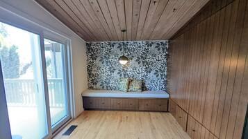 A room with a wooden floor, a bench with cushions, a wall with a floral pattern, and a window with blinds.