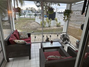 A covered patio with wicker furniture, a fan, and potted plants.