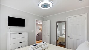 Habitación de hotel con cama, televisor, cómoda y puerta que da a otra habitación.