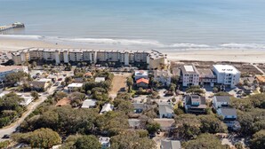 Vista aérea de un complejo turístico frente al mar, con propiedades en la playa, un muelle y una combinación de edificios residenciales y comerciales.
