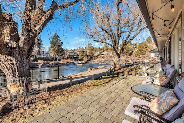 A patio with outdoor seating, a river view, and a large tree.