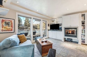 A spacious living room with a fireplace, a television, and a large window overlooking a scenic view.