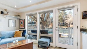 A living room with a sofa, ottoman, coffee table, and a sliding glass door leading to an outdoor patio. - Riverfront Cottage - Steam Room & Pet Friendly! (Bend)