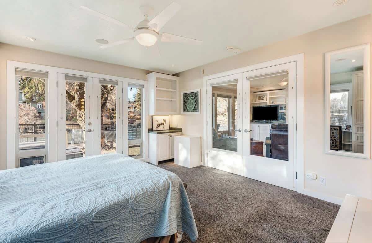Une chambre avec un lit, un ventilateur de plafond et une vue sur le jardin à travers des portes vitrées.
