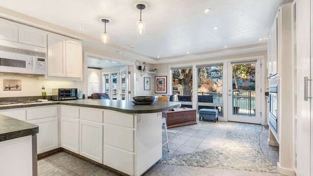 A spacious kitchen with white cabinetry, a large island, and a view to the outdoors. - Riverfront Cottage - Steam Room & Pet Friendly! (Bend)
