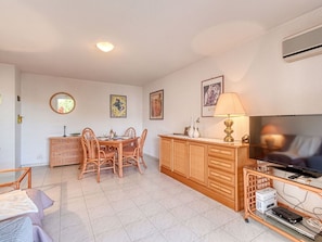 Uma sala de estar com área de jantar, móveis de madeira, uma televisão e um abajur.