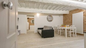 Ein gemütliches Zimmer mit Holzboden, einer schwarzen Couch, einem Esstisch mit Stühlen und einer weißen Heizung.