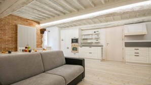 Ein modernes Wohnzimmer mit einer Couch, einer Küchenzeile mit weißen Schränken und einer Ziegelwand.