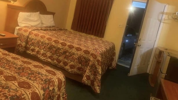 A hotel room with two beds, a nightstand, a lamp, a window with curtains, and a door leading to a balcony. - Economy INN poteau (Poteau)