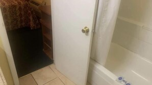 A bathroom with a white bathtub, a shower area, and a door leading to a bedroom. - Economy INN poteau (Poteau)