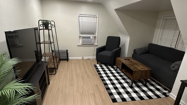 Un espace de vie compact comprenant un canapé, un fauteuil et une table basse. Un tapis à carreaux noirs et blancs recouvre le sol.