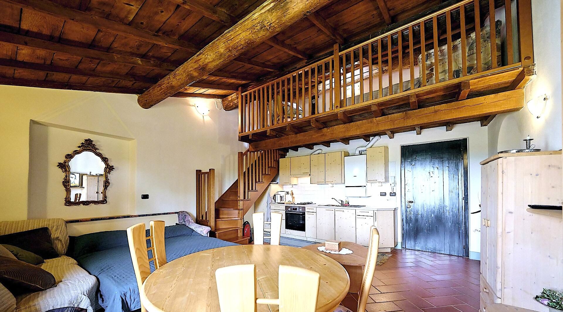 A spacious living area with a wooden ceiling, a dining table, and a kitchen area with a staircase leading to an upper level.