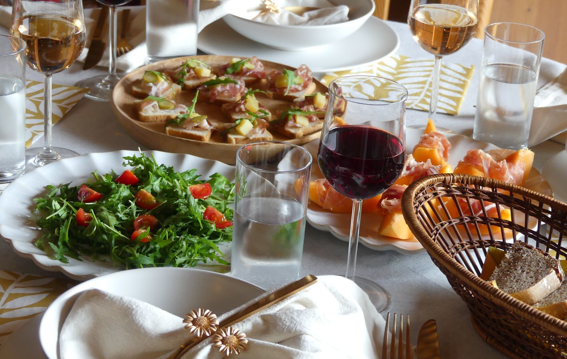 Una mesa servida con platos de comida, copas de vino y una cesta de pan.