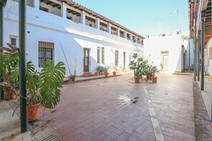 Um pátio com vasos de plantas, piso de azulejos e um edifício branco com várias janelas e sacadas.