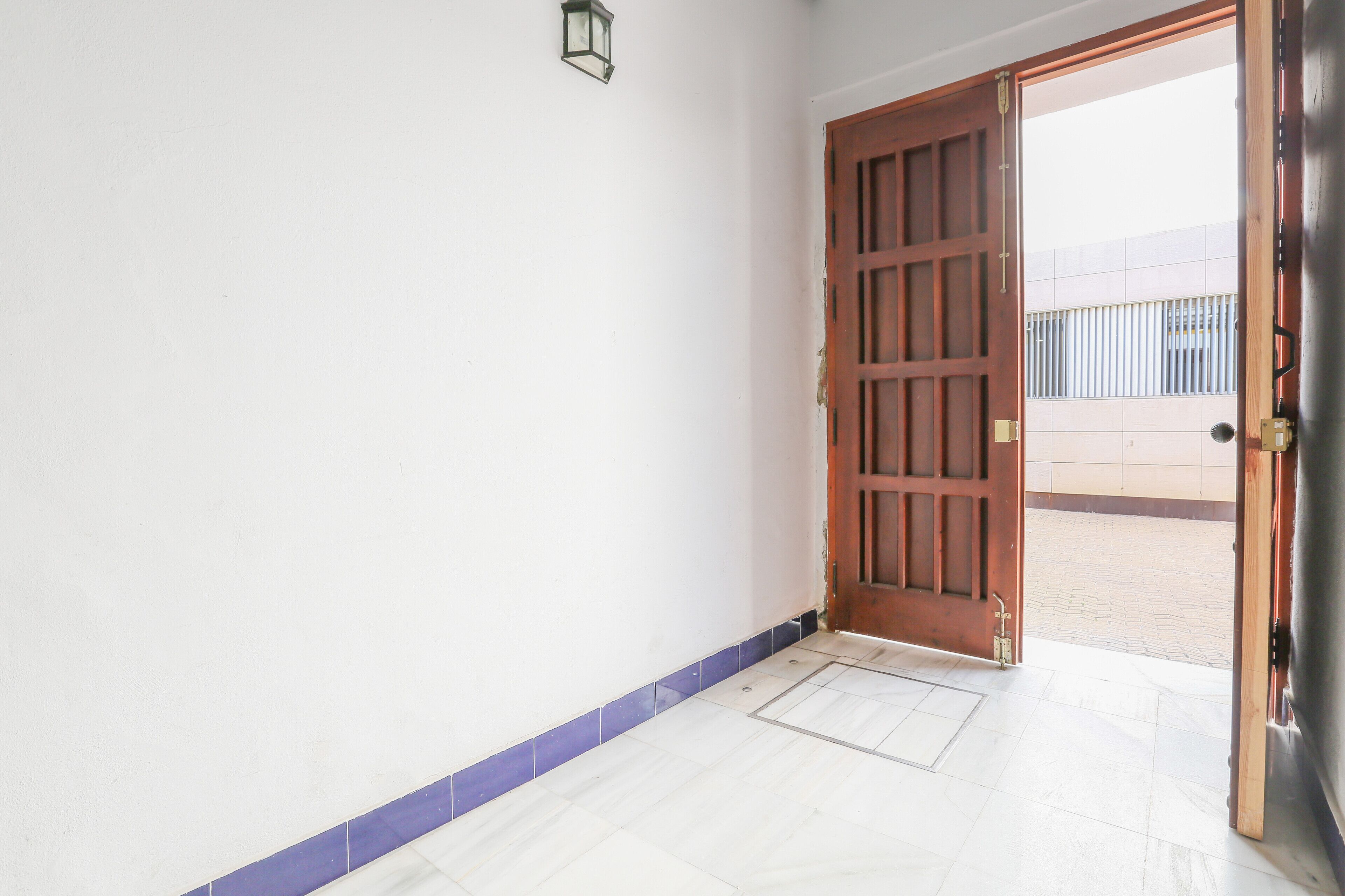 A hallway with a wooden door leading outside, a tiled floor, and a wall-mounted light fixture.