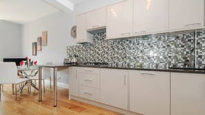 A modern kitchen with white cabinets, a tiled backsplash, and a wooden floor.