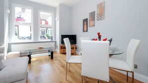 A modern living room with a glass coffee table, white sofas, a TV, and artwork on the wall.