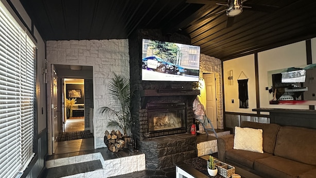 A modern living room with a stone fireplace, a flat-screen TV mounted on the wall, and a comfortable seating area with a sofa and a coffee table. - Cozy Cove with Beach, Dock, and Indoor Sauna (Sunrise Beach)
