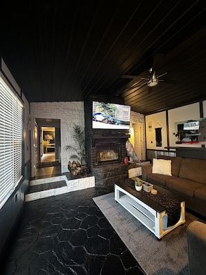 A modern living room with a stone fireplace, a flat-screen TV mounted on the wall, and a comfortable seating area with a sofa and a coffee table. - Cozy Cove with Beach, Dock, and Indoor Sauna (Sunrise Beach)