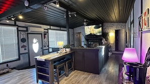 A modern kitchen with a central island, a bar area with a coffee machine, and a large TV screen. - Cozy Cove with Beach, Dock, and Indoor Sauna (Sunrise Beach)