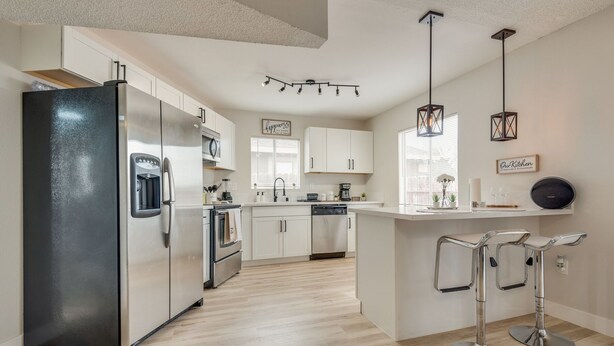A modern kitchen with stainless steel appliances, white cabinetry, and a central island with bar stools. - Cozy home! 18 min away from Strip and Fremont! (North Las Vegas)