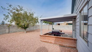 A covered patio area with a barbecue grill, a table, and a brick wall. - Cozy home! 18 min away from Strip and Fremont! (North Las Vegas)