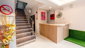 A reception area with a wooden counter, a green seating area, a staircase, and a no-smoking sign. - Taj Grand Hotel (Malacca City)